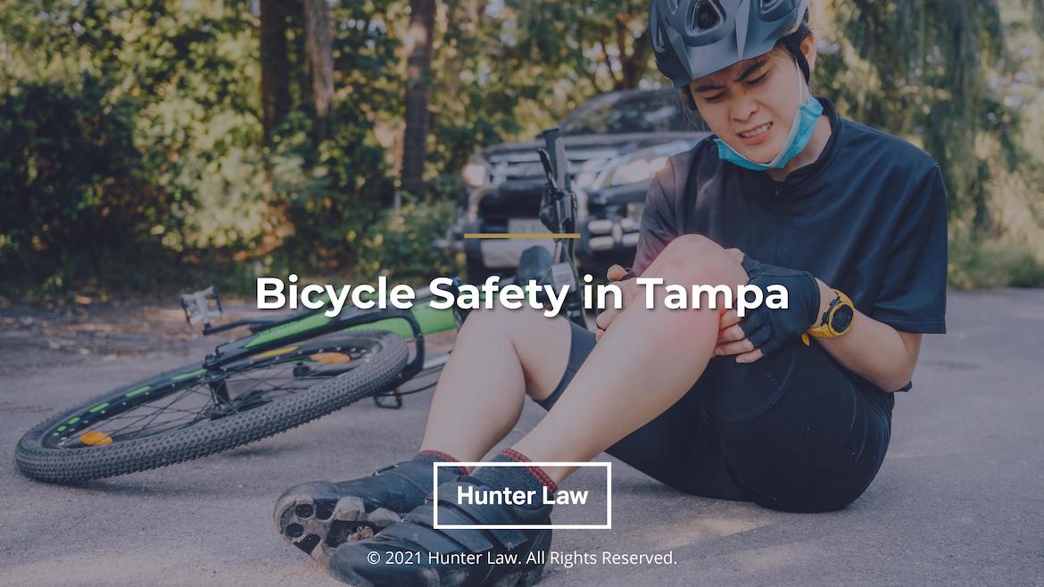 Person sitting on pavement holding knee with bicycle on ground with title: Bicycle Safety in Tampa