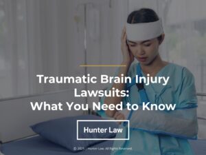 Featured: Female sitting on hospital bed holding her hand to her bandaged forehead- Traumatic Brain Injury Lawsuits: What You Need to Know.